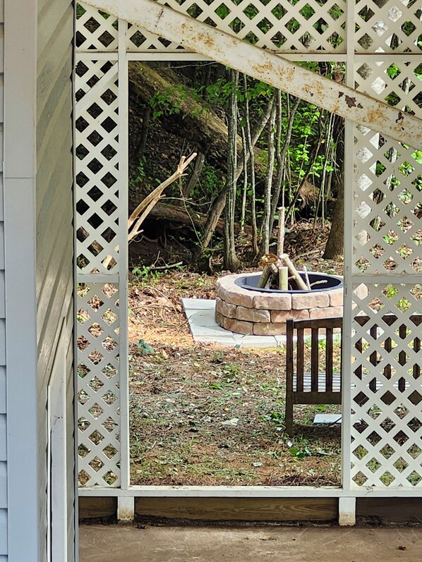 A wooden bench under a white lattice structure with a stone fire pit in the background.