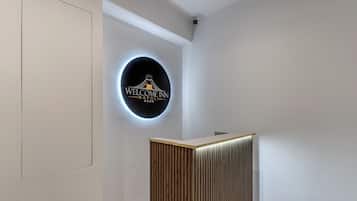 Un'area reception con un cartello circolare che indica 'Welcome Inn Napoli Room' e un bancone reception in legno.