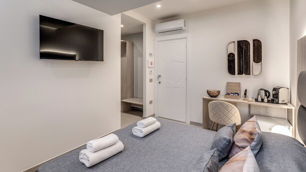 Ein modernes Hotelzimmer mit einem Bett, einem Flachbildfernseher, einem Schreibtisch mit Kaffeemaschine und einer Tür zu einem Badezimmer.