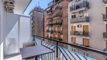 Un balcone con tavolo e sedie, affaccia su una fila di edifici a più piani con balconi e condizionatori d'aria.