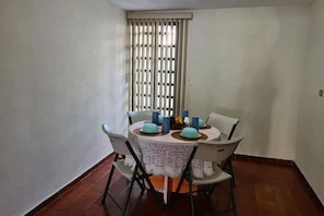 A dining area with a round table, four chairs, and a window with vertical blinds.