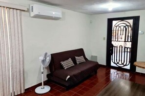 A living room with a brown sofa, a standing fan, and a window with curtains. - Central house, 5 min. by car from TEC; inverter AC, parking, pet-friendly (Monterrey)