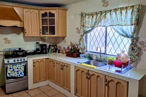 A kitchen with wooden cabinets, a stove, and a window with floral curtains. - Central house, 5 min. by car from TEC; inverter AC, parking, pet-friendly (Monterrey)