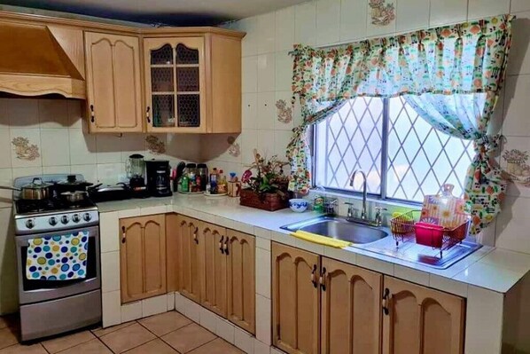 A kitchen with wooden cabinets, a stove, and a window with floral curtains.