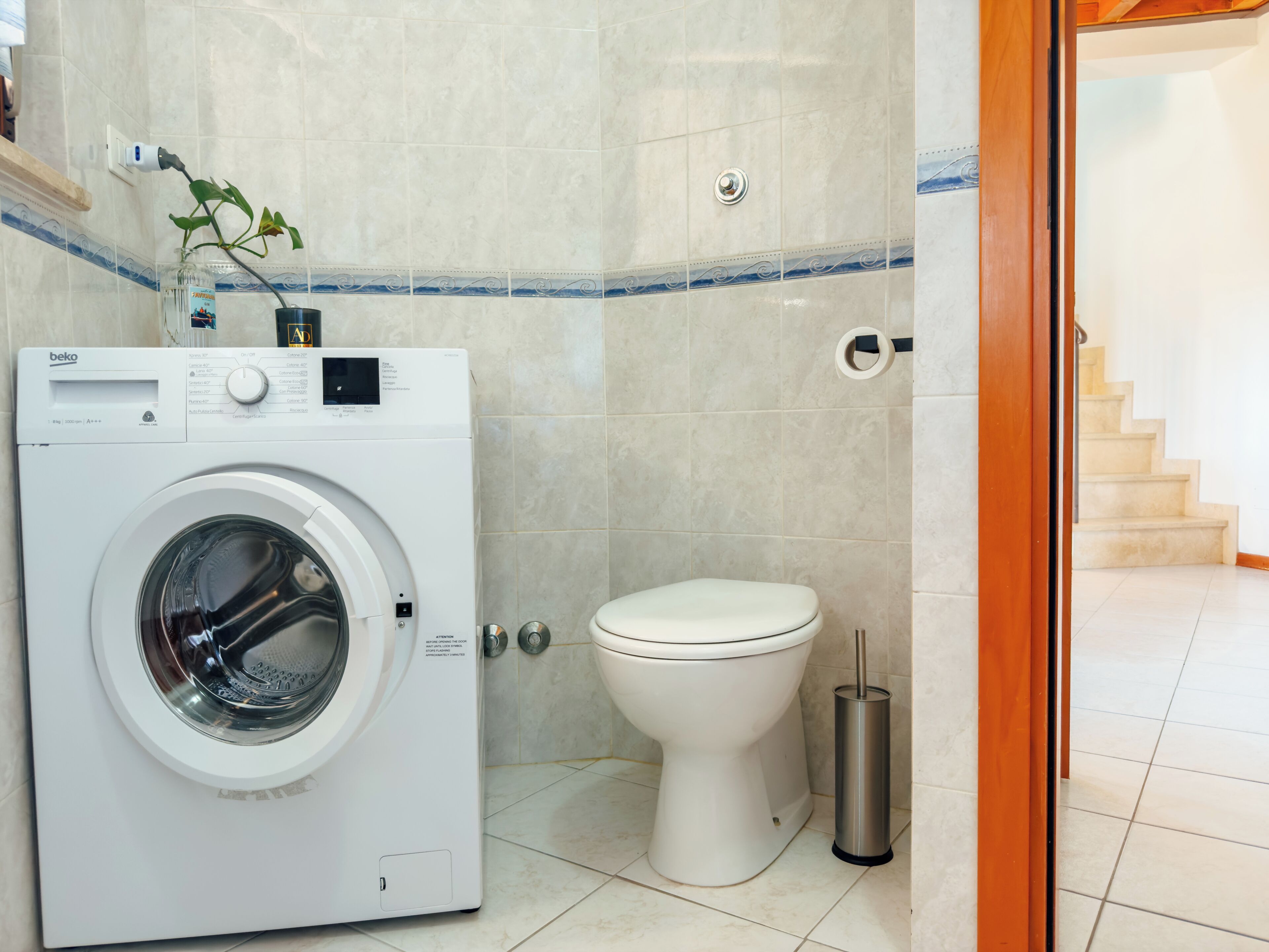 Une petite salle de bain équipée d’un lave-linge, de toilettes et d’une poubelle.