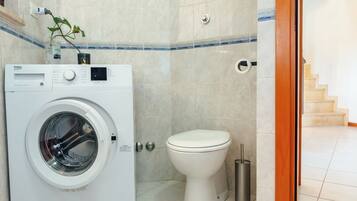Une petite salle de bain équipée d’un lave-linge, de toilettes et d’une poubelle.