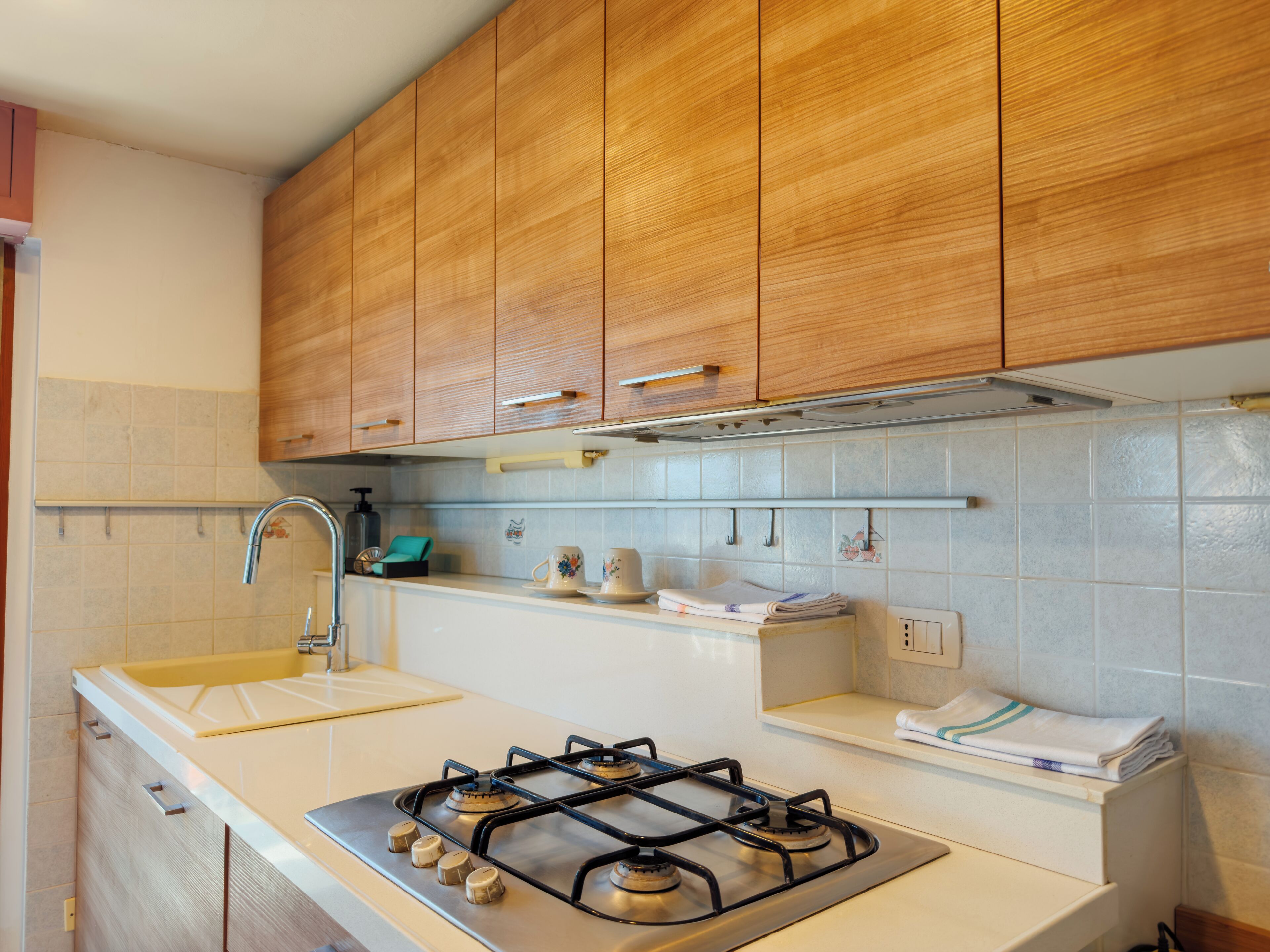 Una cocina con armarios de madera, estufa a gas, lavamanos y salpicadero de azulejos.