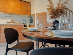 A modern kitchen with wooden cabinets, a dining table set for two with chairs, and a vase with dried plants.