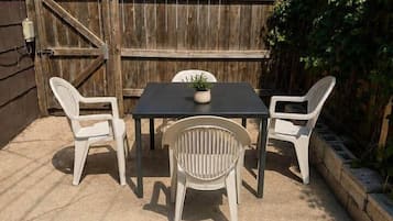 An outdoor patio with a table and four chairs, surrounded by a wooden fence and greenery.