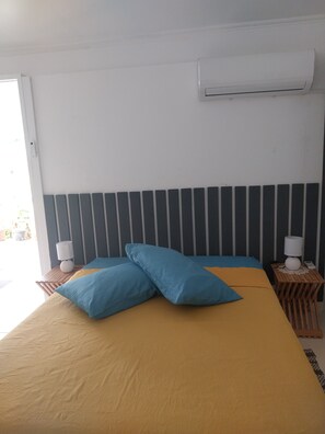 A hotel room with a bed, two bedside tables, a wall-mounted air conditioner, and a window.