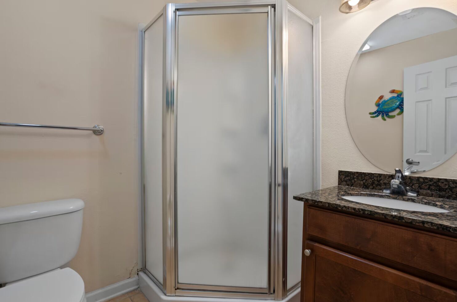 Baño con ducha envuelta en vidrio, inodoro, lavabo con encimera de granito y mueble de madera.