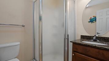 Baño con ducha envuelta en vidrio, inodoro, lavabo con encimera de granito y mueble de madera.