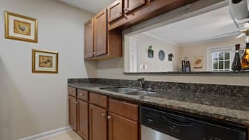 A kitchen with wooden cabinets, a granite countertop, a dishwasher, and a large mirror above the sink.