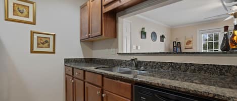 A kitchen with wooden cabinets, a granite countertop, a dishwasher, and a large mirror above the sink.