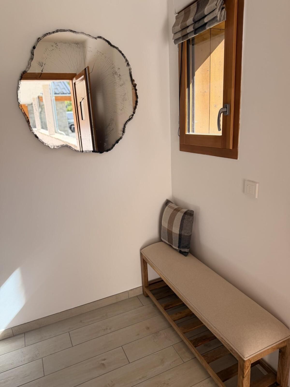 A room with a wooden bench, a mirror with a damaged section, and a window with a curtain.