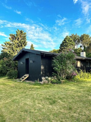 A single-story wooden building with a dark exterior, a small porch, and a clear sky.
