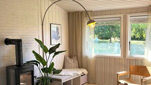 Um quarto acolhedor com uma lareira a lenha, um banco, uma cadeira e uma janela grande com vista para o verde.