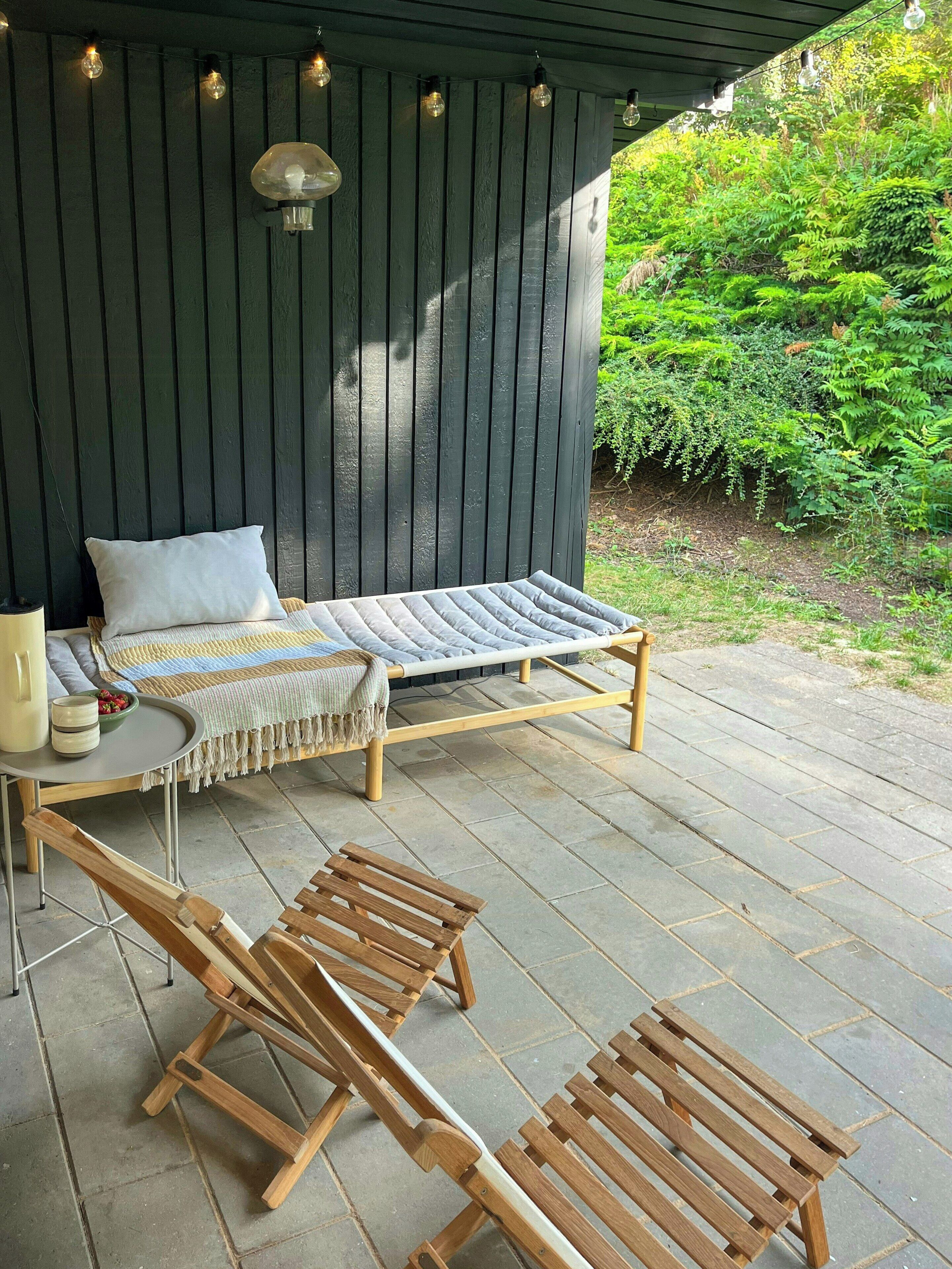 Una terraza de madera con una hamaca, dos sillas de madera y una mesa con una lámpara y adornos.
