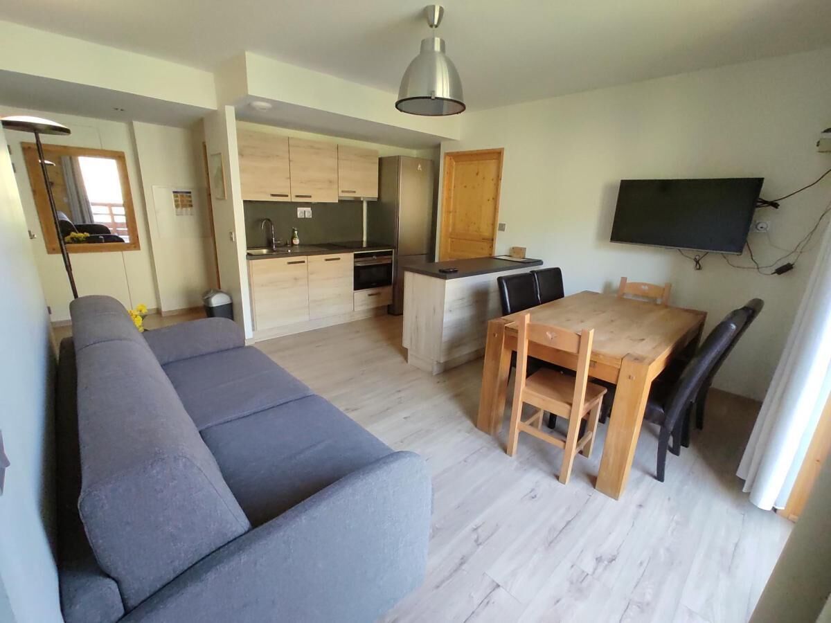 Un espace de vie moderne comprenant un canapé, une table à manger, des chaises, un coin cuisine et un téléviseur à écran plat fixé au mur.