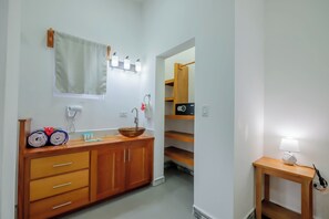 A bathroom with a wooden vanity, a sink, a mirror, a towel rack, a toilet, and a small table with a lamp.