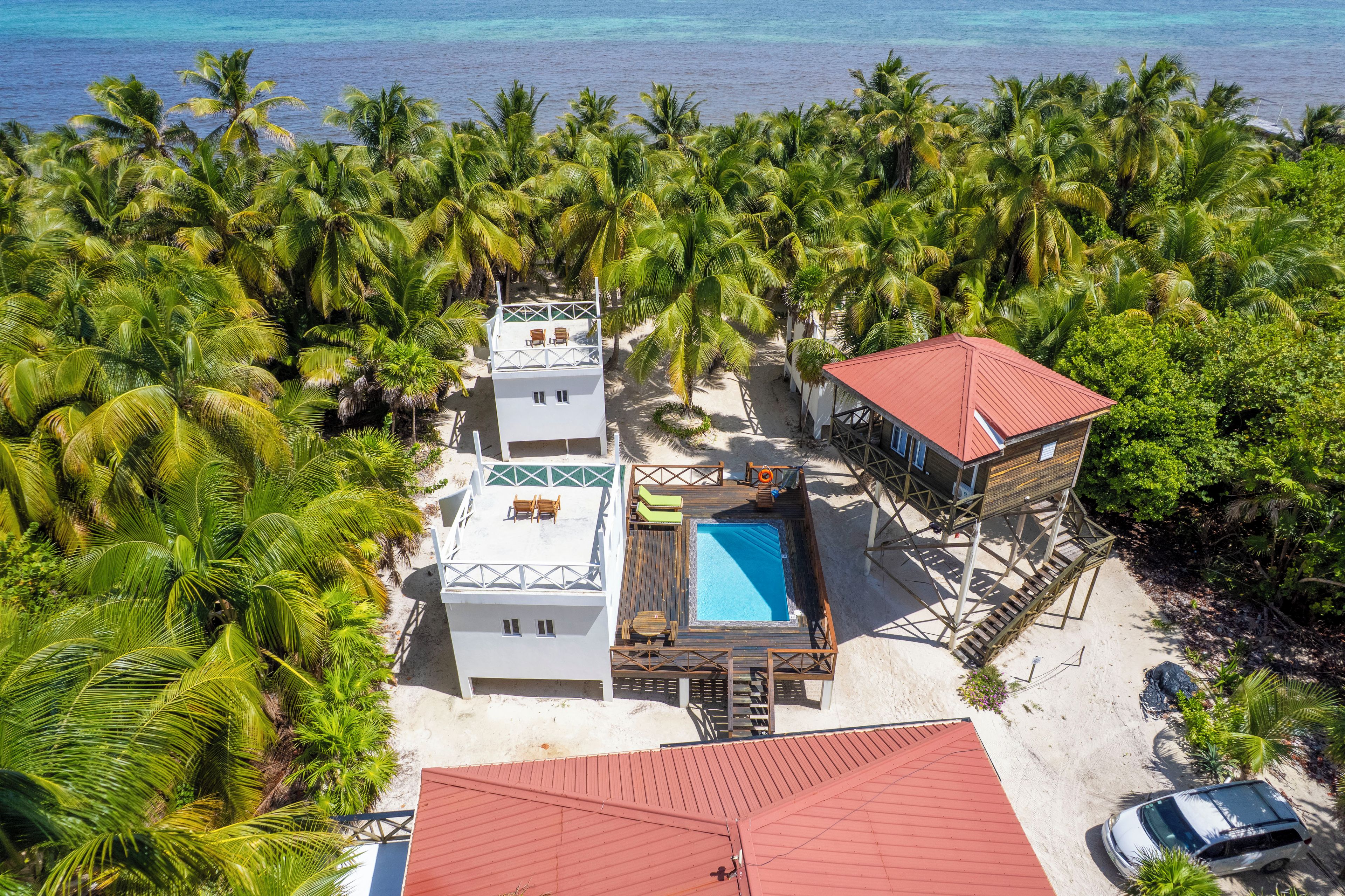 A beachfront property with multiple buildings, a swimming pool, and a red-roofed structure.