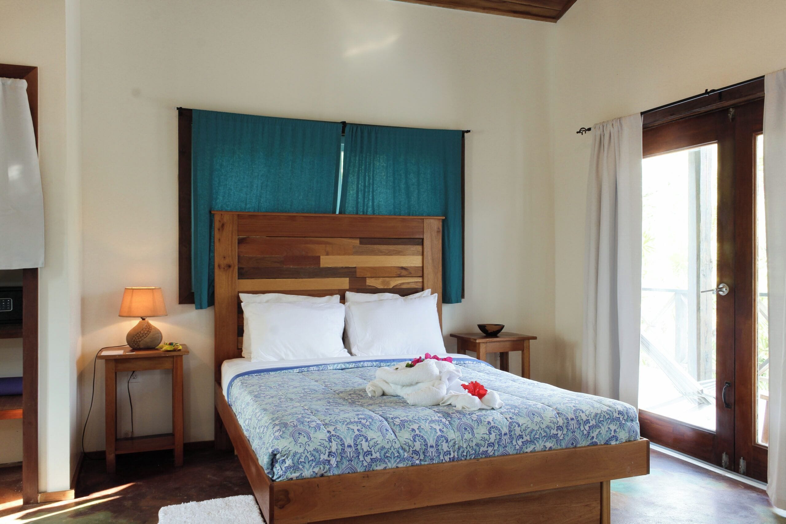 Un dormitorio con una cama de madera, una mesita de noche con lámpara, una ventana con cortinas y vistas al exterior.