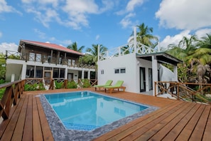 A pool area with wooden deck, lounge chairs, and a building with a red roof.