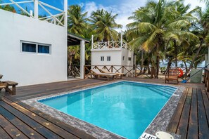 A pool area with wooden deck, lounge chairs, and a white building with windows.