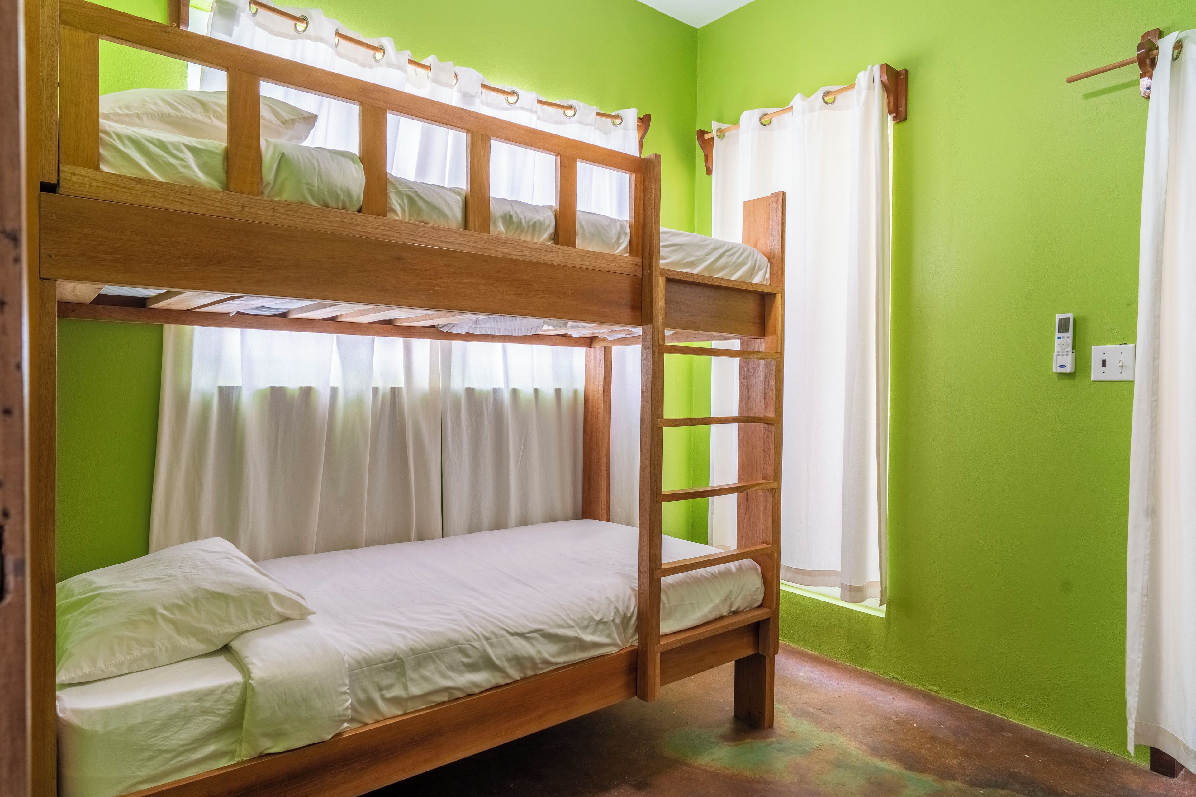 A bunk bed room with a ladder, a window with curtains, and a power outlet on the wall.