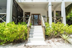 Una escalera que lleva a una puerta, rodeada de follaje y suelo arenoso.