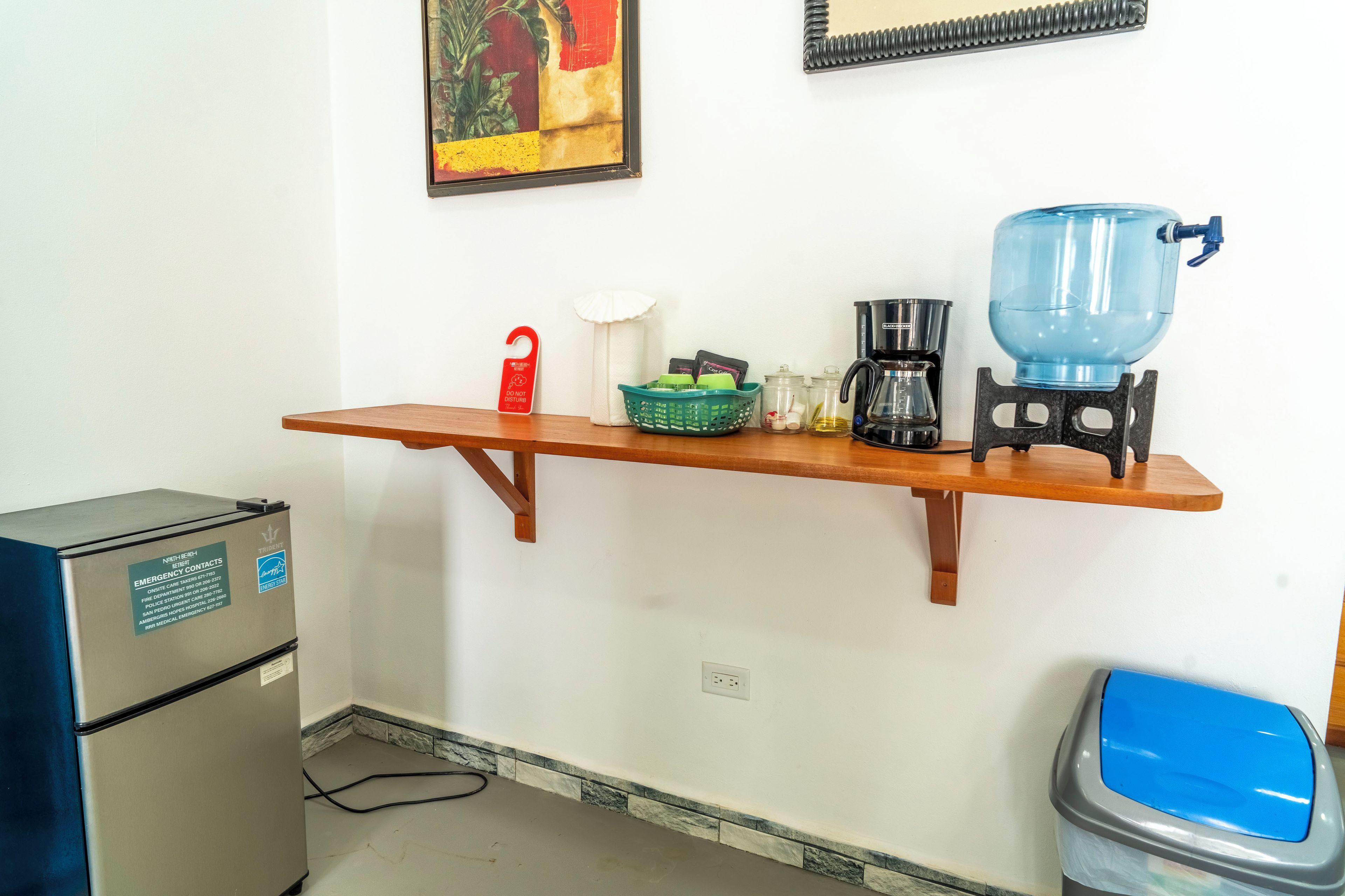Une petite cuisine équipée d’un réfrigérateur, d’une machine à café, d’un distributeur d’eau et d’une poubelle.