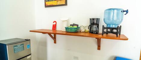 Une petite cuisine équipée d’un réfrigérateur, d’une machine à café, d’un distributeur d’eau et d’une poubelle.