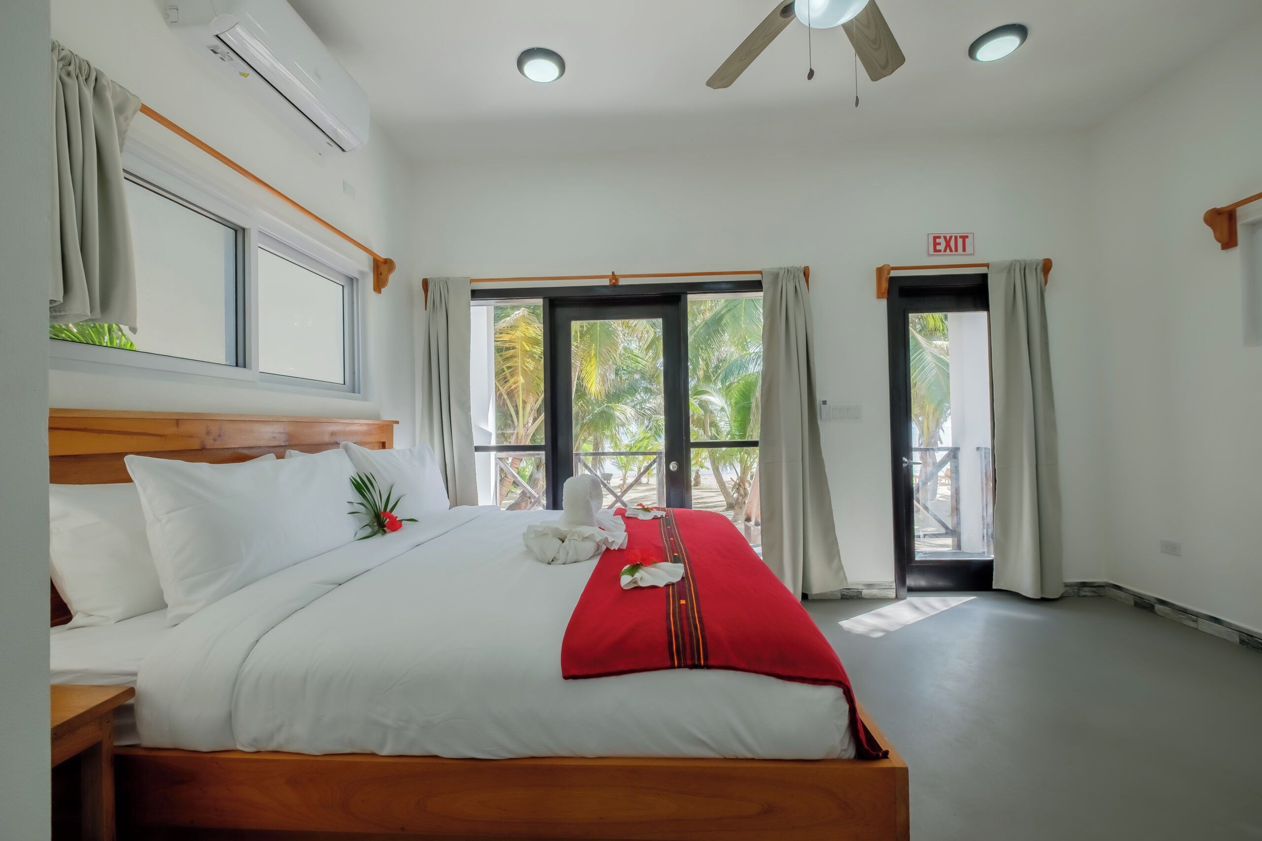 A hotel room with a bed, a ceiling fan, and large windows.