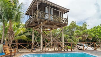 Une structure en bois dotée d’un balcon, d’une piscine et entourée d’une végétation tropicale.