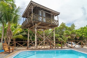 A wooden structure with a balcony, a pool, and surrounding tropical vegetation.