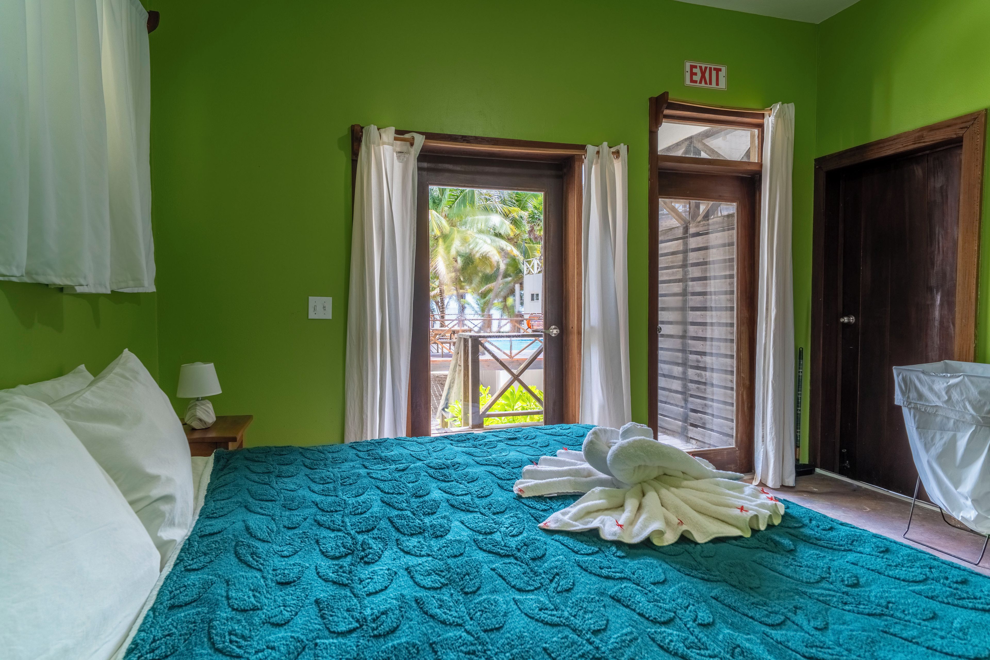 Une chambre d’hôtel avec un lit, une table de chevet, une lampe et une vue sur la piscine par la fenêtre.