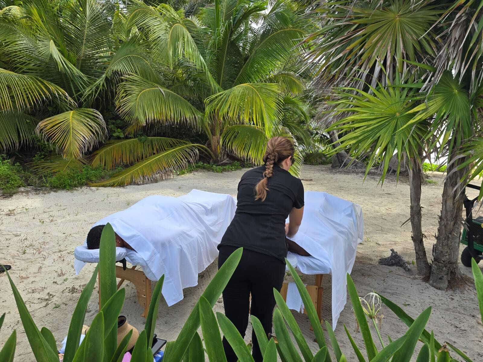 A massage table set up on a sandy beach with palm trees in the background.