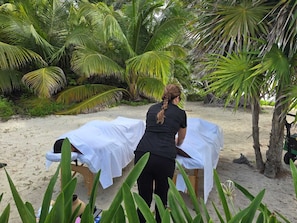 A massage table set up on a sandy beach with palm trees in the background.
