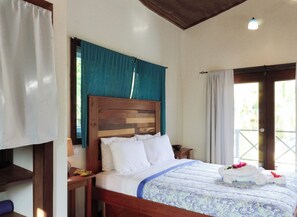 A hotel room with a wooden headboard, a bed with white linens, a blue patterned bedspread, and a view through a door.