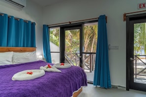 A hotel room with a bed, a window with curtains, and a view of palm trees.