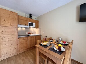 A compact kitchen with wooden cabinets, a microwave, and a dining table set with plates, glasses, and fruits. - 50m from ski slopes, 2nd floor, swimming pool, balcony, ski locker, 32m², Vars (Vars)