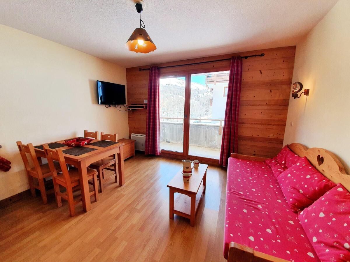 Une pièce comprenant une table à manger en bois, des chaises, un canapé, un téléviseur et une fenêtre avec des rideaux.