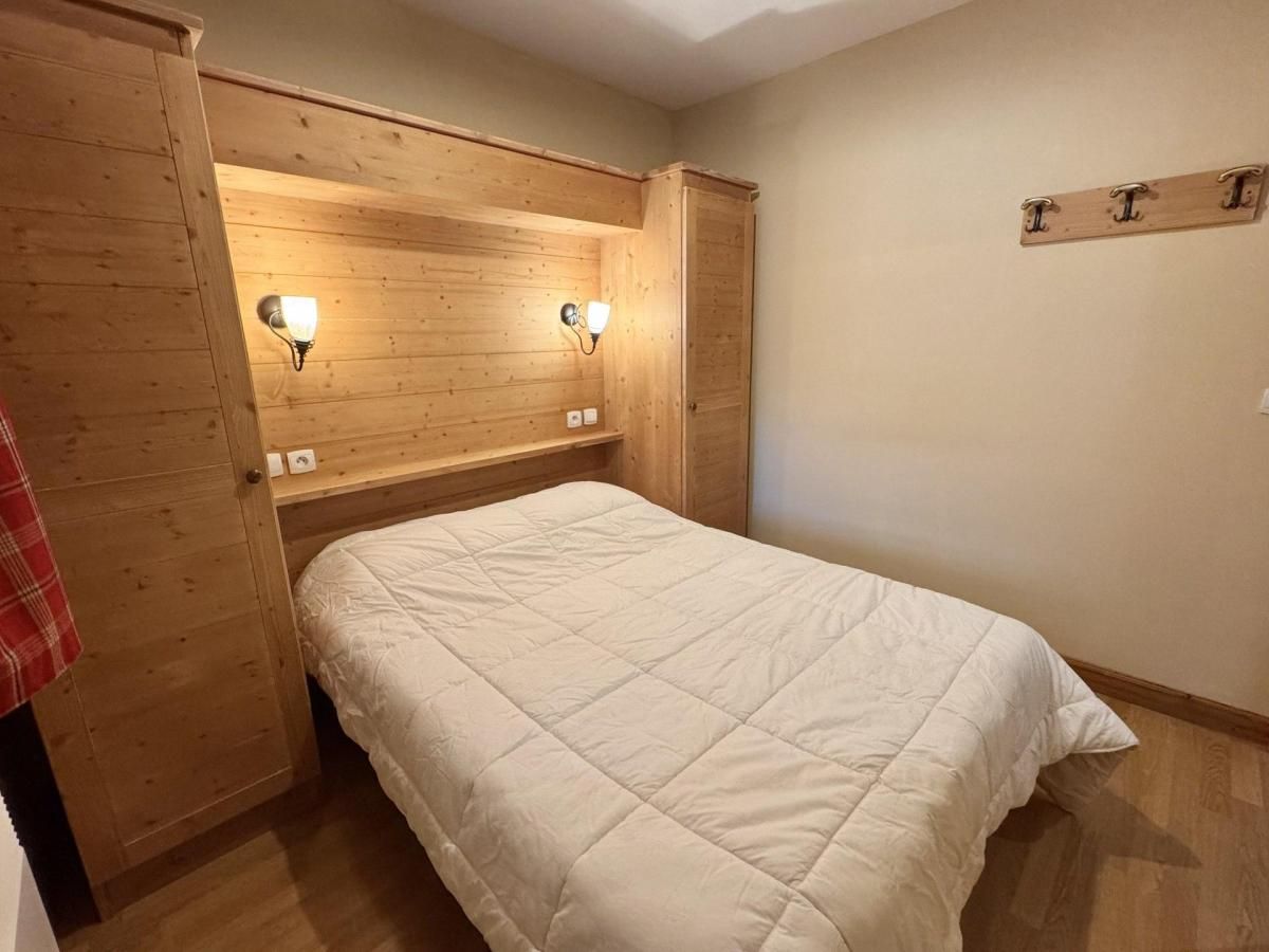 Een slaapkamer met een bed, houten hoofdbord, wandlampen en een houten kapstok.