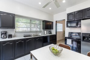 A modern kitchen with dark cabinetry, a white countertop, a ceiling fan, and a dining area with a table and chairs. - Private Mansion - Pool - Mins to Beach (Hollywood)
