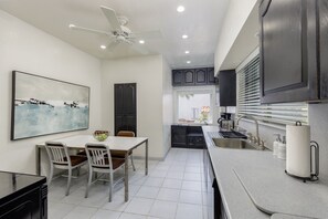 A modern kitchen with a dining area, white tiled floor, dark cabinets, and a ceiling fan. - Private Mansion - Pool - Mins to Beach (Hollywood)