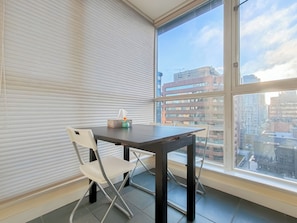 Une pièce avec une table et une chaise, une fenêtre donnant sur des immeubles et un store fermé.
