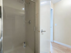 Une douche fermée par des parois en verre, dotée d’un pommeau de douche à main, d’un flacon de savon liquide et d’une porte avec une poignée moderne.
