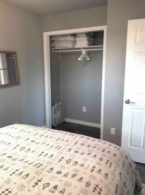 Une chambre à coucher avec un lit, une armoire où sont suspendus des vêtements, un radiateur et une porte.