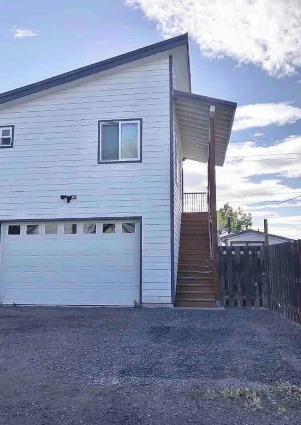 Une maison de plain-pied avec un garage, un petit porche doté d’un escalier en bois et une clôture en bois en arrière-plan.