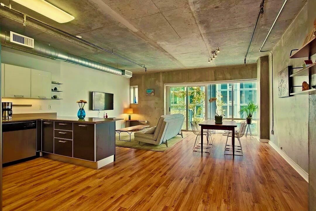 A modern kitchen with a central island, a dining area with a table and chairs, and a large window providing natural light.